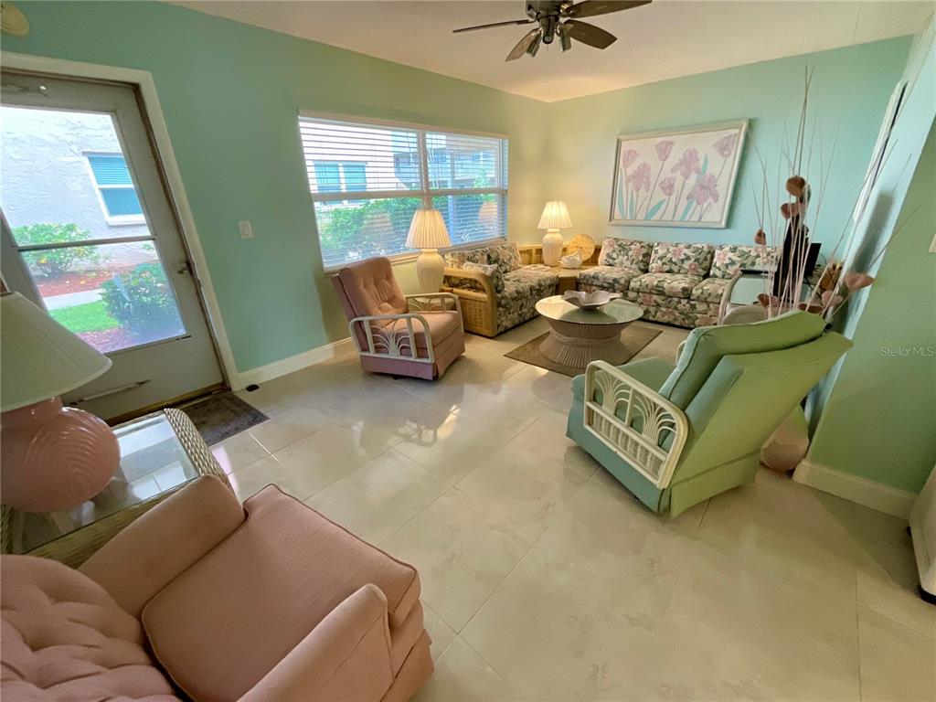 A living room features light green walls, tile flooring, floral furniture, and a ceiling fan — 10034 64TH AVENUE N UNIT 11, ST PETERSBURG, FL