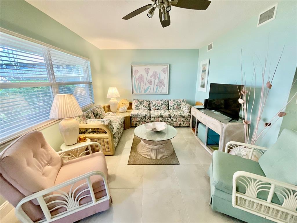 A living room features light blue walls, tile flooring, floral furniture, and a ceiling fan — 10034 64TH AVENUE N UNIT 11, ST PETERSBURG, FL