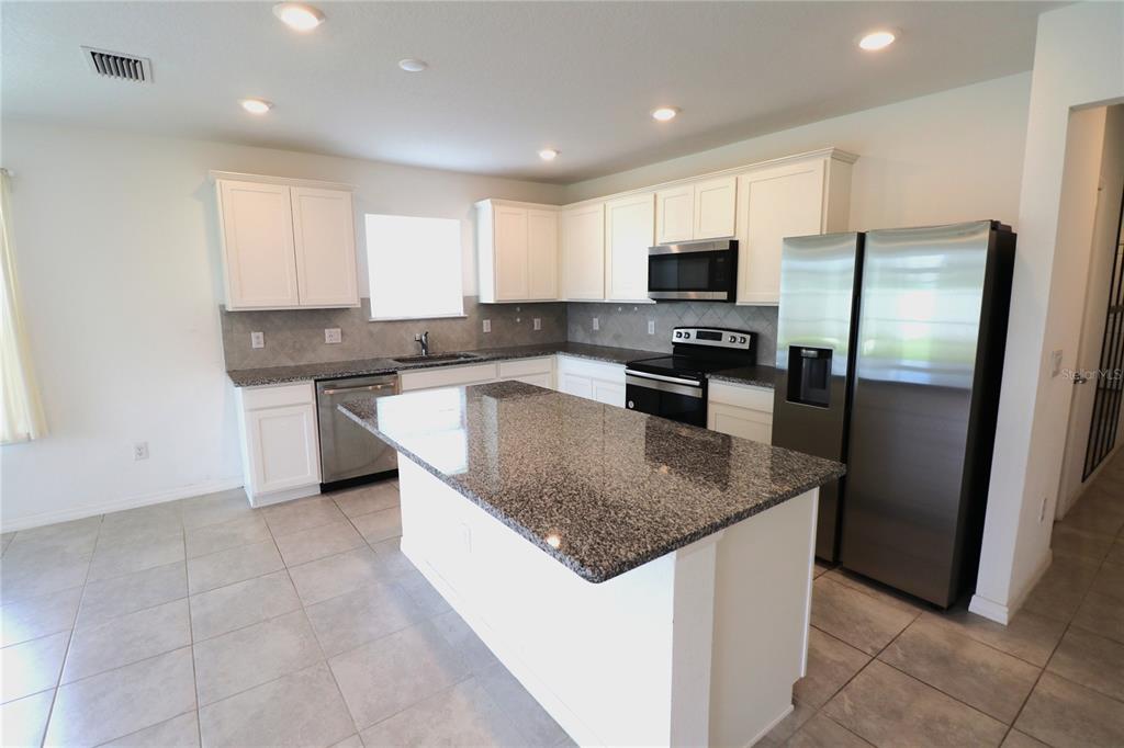 A kitchen features white cabinets, granite countertops, stainless steel appliances, and a central island — 4006 CAPRI COAST DRIVE, PLANT CITY, FL