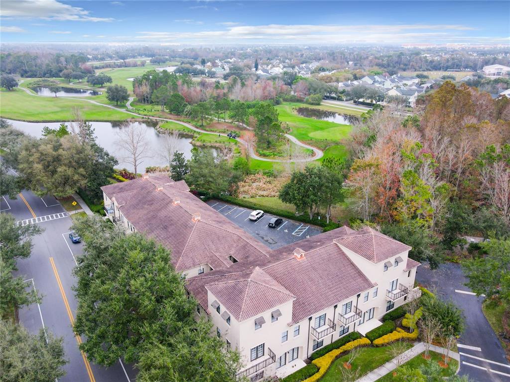 An aerial view shows a multi-story building with a tiled roof next to a golf course — 917 WATERSIDE LANE UNIT 203, CELEBRATION, FL
