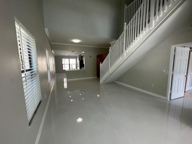 A bright, open-concept living area features white tile flooring, a staircase, and a kitchen view — 917 WATERSIDE LANE UNIT 203, CELEBRATION, FL