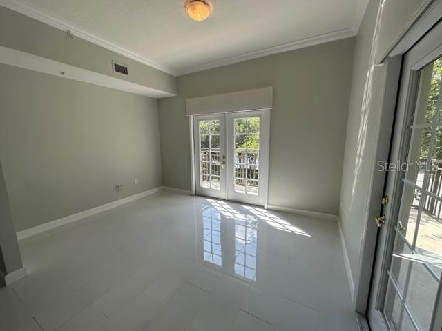 An empty room with white tile floors, crown molding, and glass doors leading to a balcony — 917 WATERSIDE LANE UNIT 203, CELEBRATION, FL