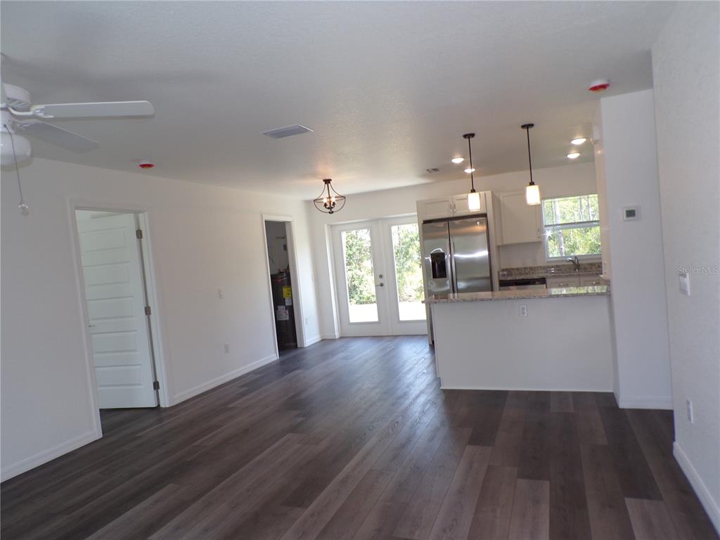 An open-concept living area features dark wood-look flooring, a kitchen with stainless appliances, and French doors — 29401 GOODHUE STREET, PUNTA GORDA, FL