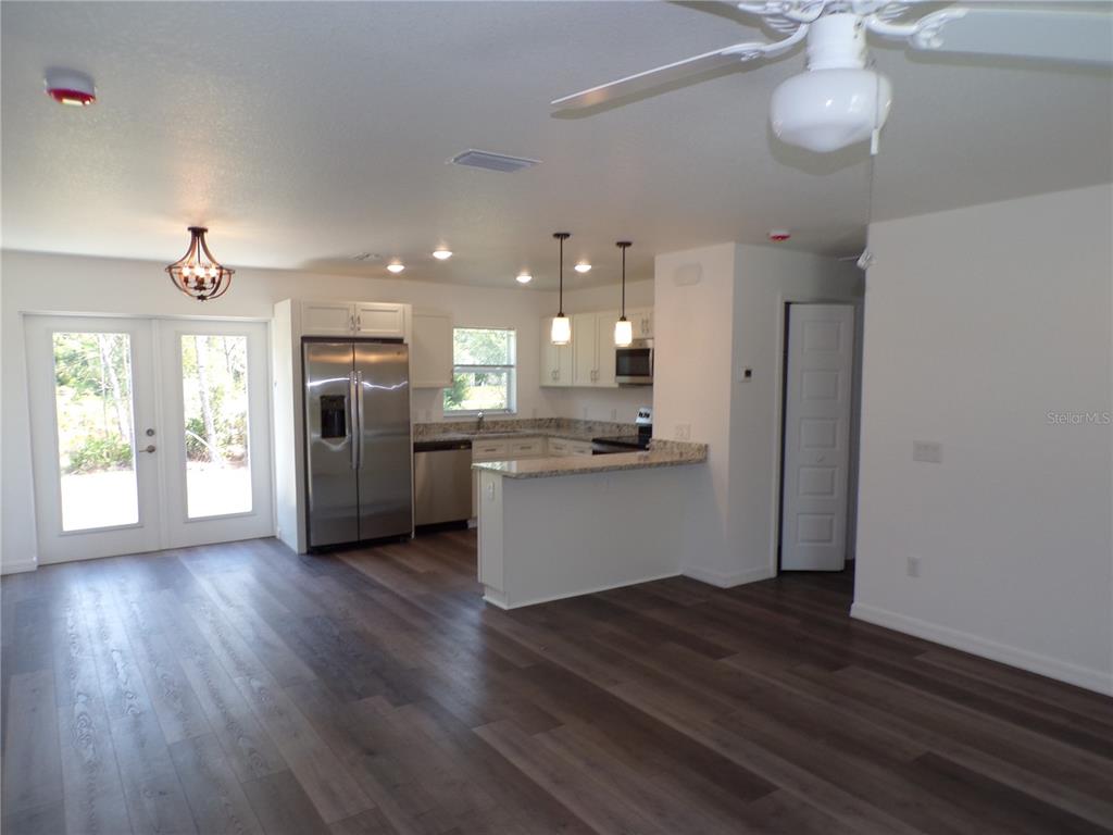 A kitchen with stainless steel appliances, white cabinets, and a peninsula opens to a living area — 29401 GOODHUE STREET, PUNTA GORDA, FL