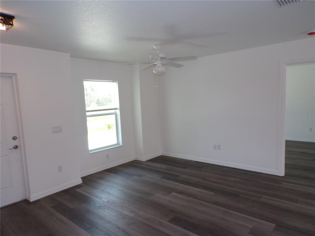 An empty room features white walls, a ceiling fan, and dark wood-look plank flooring — 29401 GOODHUE STREET, PUNTA GORDA, FL
