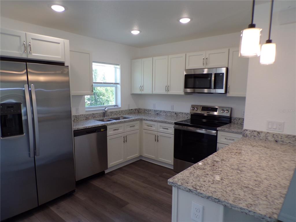 A kitchen features white cabinets, granite countertops, stainless steel appliances, and wood-look flooring — 29401 GOODHUE STREET, PUNTA GORDA, FL