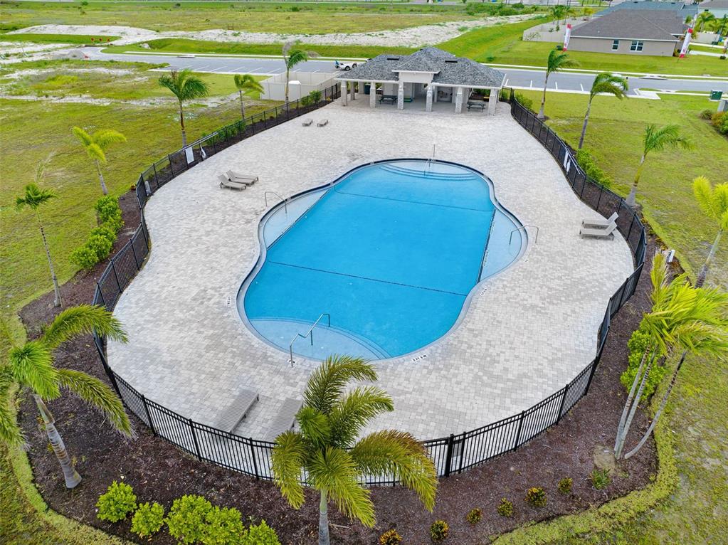 An aerial view shows a fenced swimming pool with a covered patio area and palm trees — 2530 ROYGARIS STREET NW, PALM BAY, FL