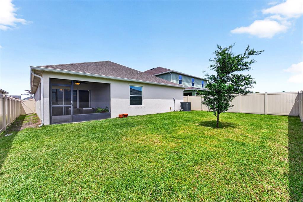 A backyard with a screened-in patio, a single tree, and a tan vinyl privacy fence — 2530 ROYGARIS STREET NW, PALM BAY, FL