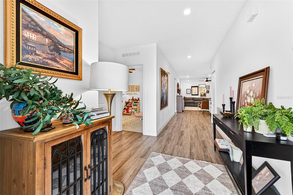 A hallway with wood-look flooring connects a foyer with a console table to a living area — 2530 ROYGARIS STREET NW, PALM BAY, FL