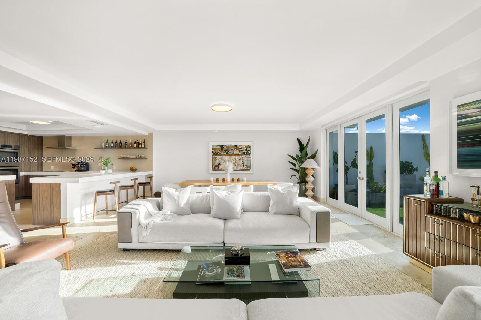 A bright living room features a white sofa, glass coffee table, and an open kitchen — 5600 Collins Ave # D, Miami Beach FL 33140, MIAMI BEACH, FL
