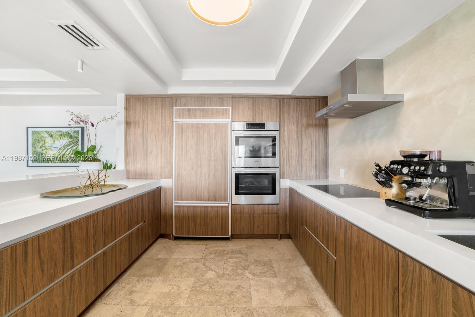 A modern kitchen features wood-grain cabinetry, white countertops, stainless steel appliances, and stone flooring — 5600 Collins Ave # D, Miami Beach FL 33140, MIAMI BEACH, FL