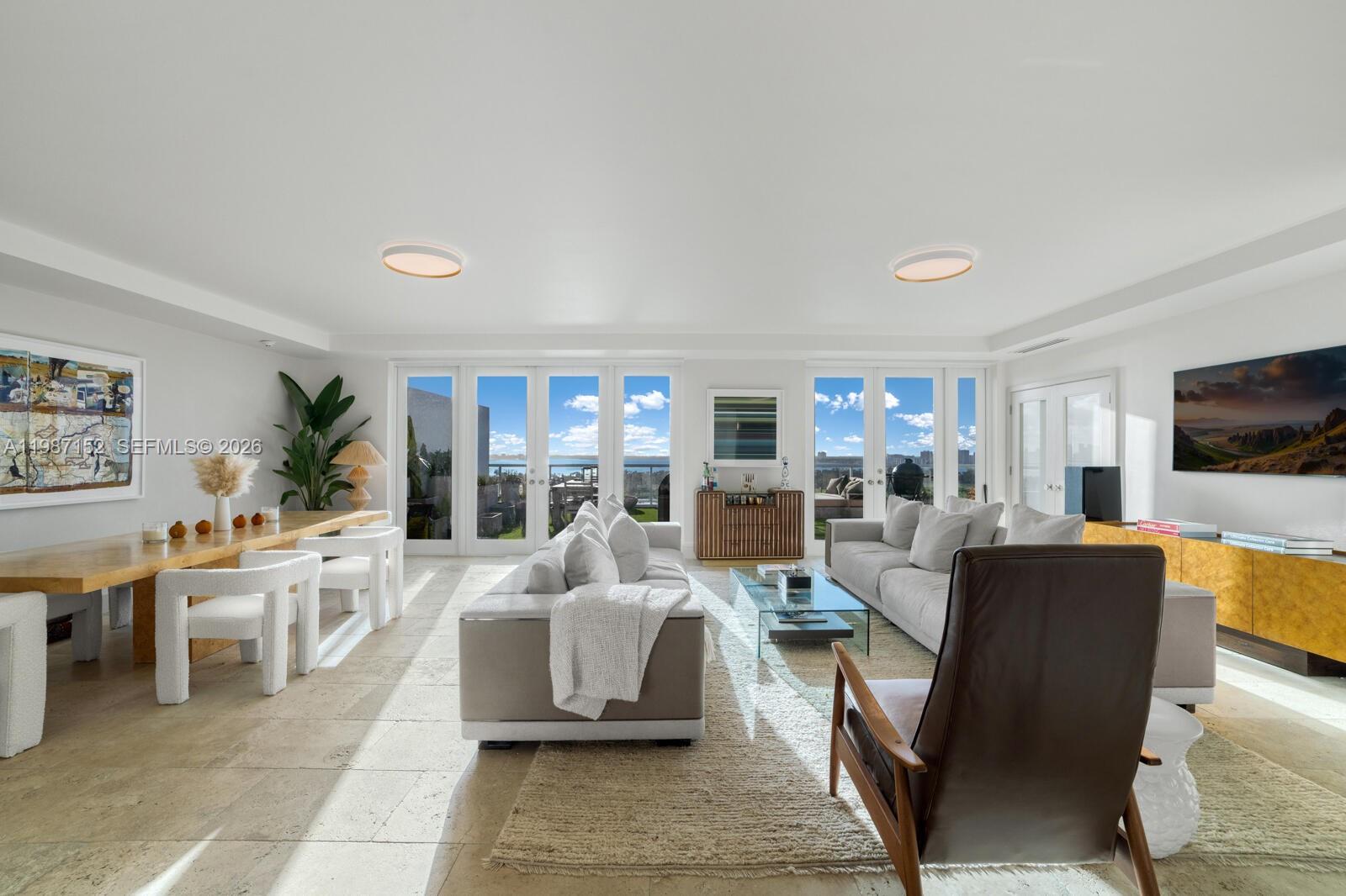 A bright, open-concept living and dining area features stone floors and large glass balcony doors — 5600 Collins Ave # D, Miami Beach FL 33140, MIAMI BEACH, FL