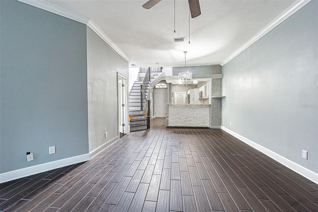 A living area with dark wood-look tile floors, a staircase, and a kitchen breakfast bar — 6400 46TH AVENUE N UNIT 3, KENNETH CITY, FL