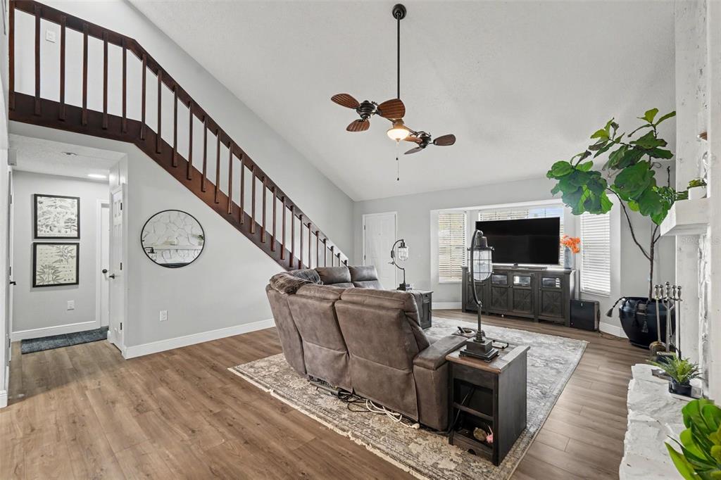 A living room features wood-look flooring, a vaulted ceiling, a staircase, and a gray sofa — 736 SANDY CREEK DRIVE, BRANDON, FL
