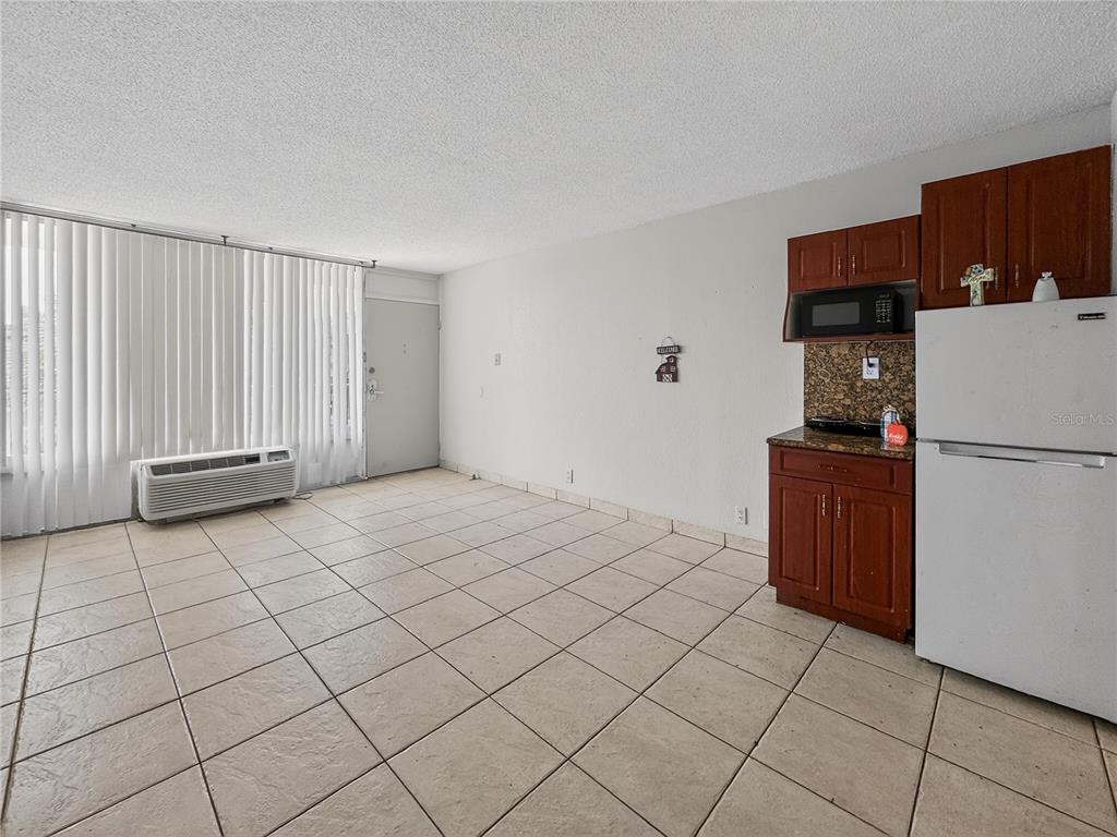 A small kitchen area with wooden cabinets and a white refrigerator in a tiled room — 7900 S ORANGE BLOSSOM TRAIL UNIT 2066, ORLANDO, FL