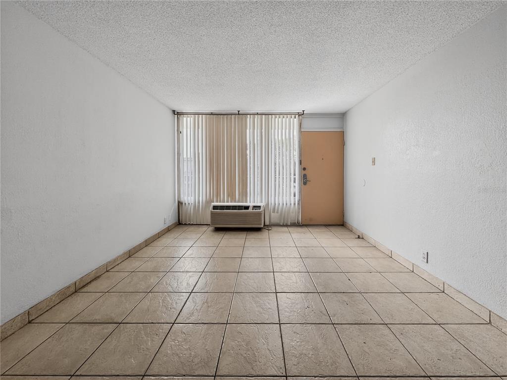 An empty room with beige tile flooring, white walls, a window with vertical blinds, and an AC unit — 7900 S ORANGE BLOSSOM TRAIL UNIT 2066, ORLANDO, FL