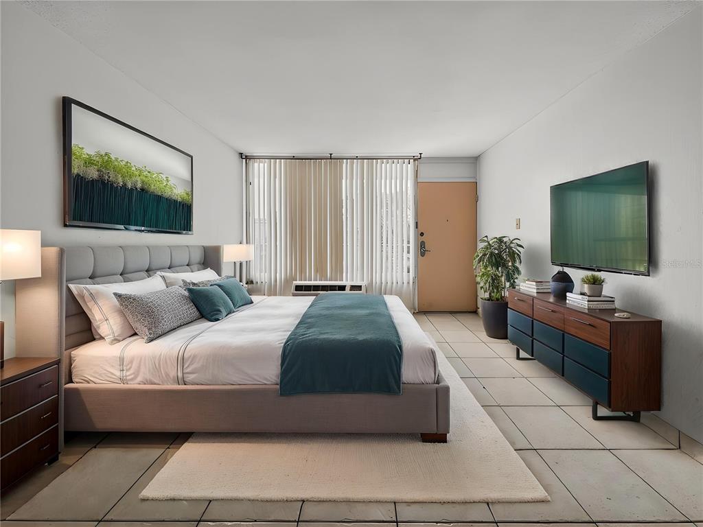 A bedroom features a gray upholstered bed, a television on a dresser, and tile flooring — 7900 S ORANGE BLOSSOM TRAIL UNIT 2066, ORLANDO, FL