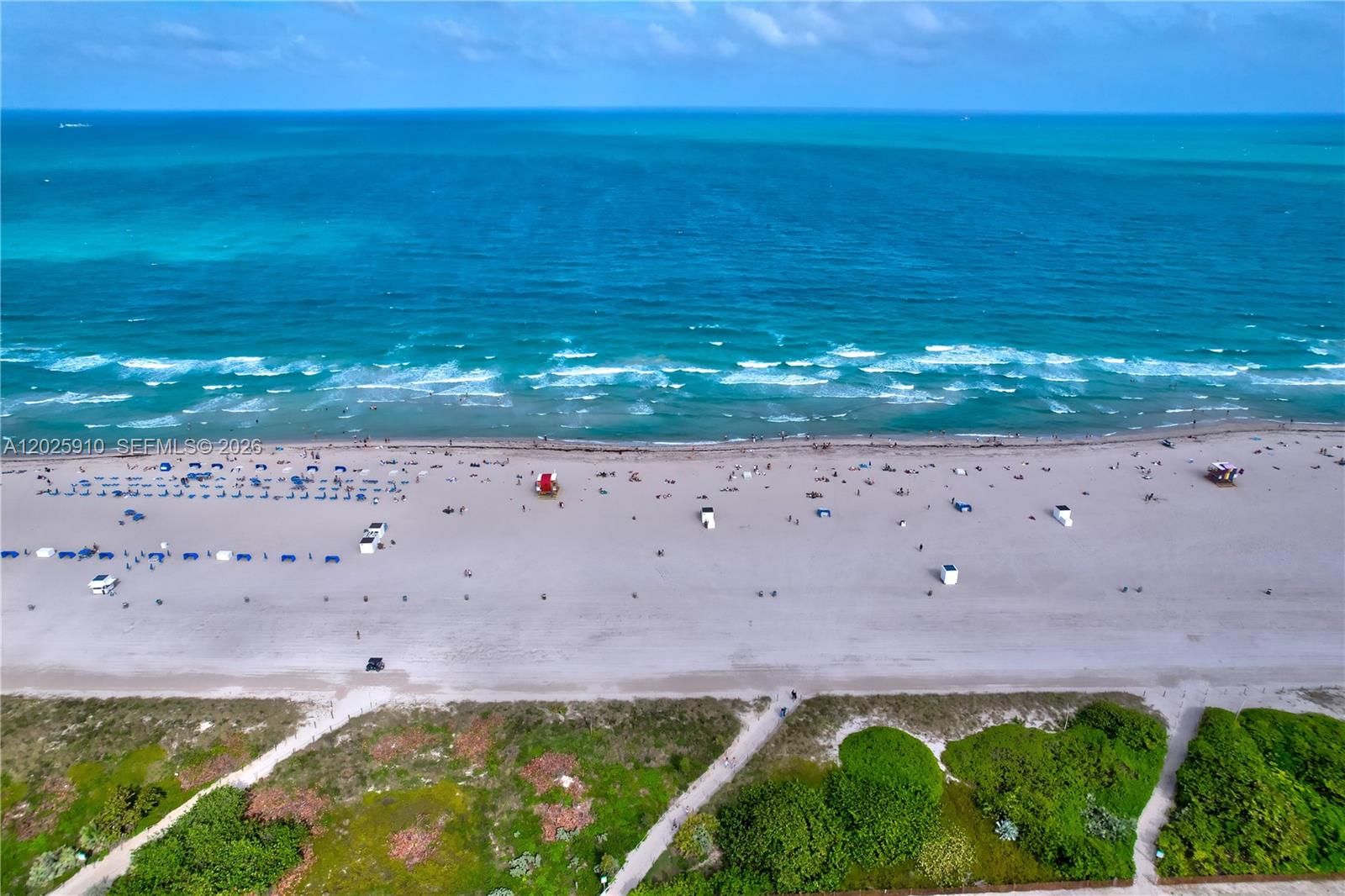 An aerial view shows a sandy beach with umbrellas, lifeguard stands, and the ocean — 1255 Collins Ave # 504, Miami Beach FL 33139, MIAMI BEACH, FL
