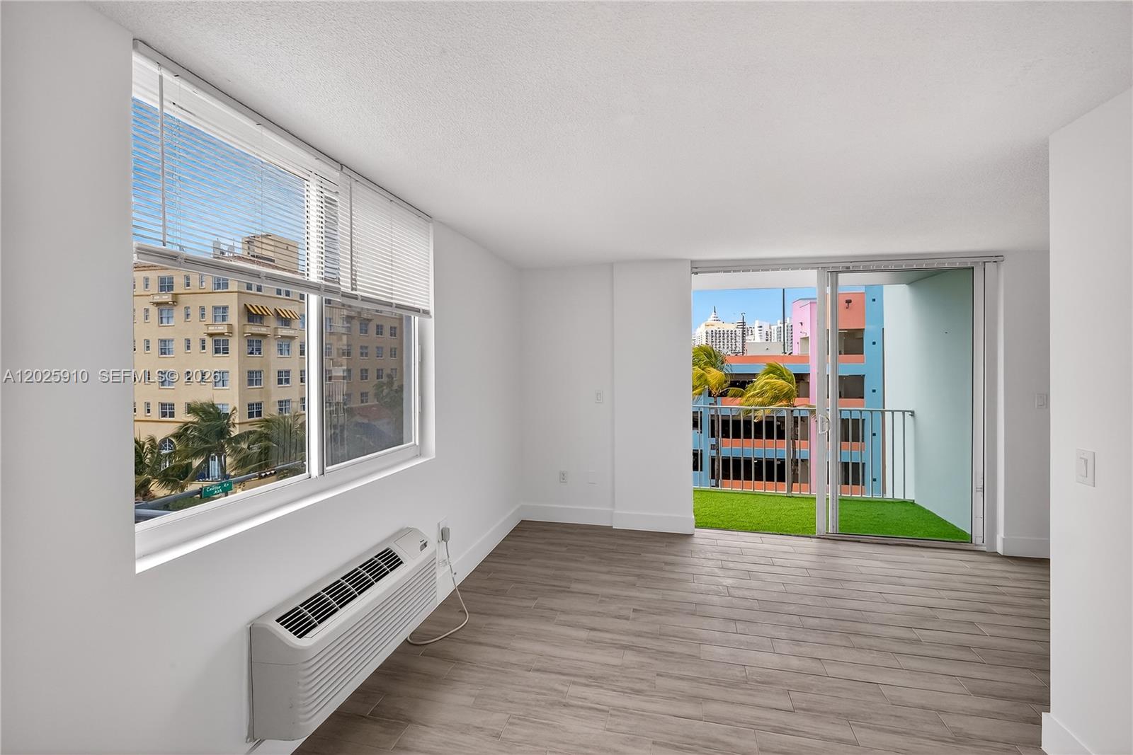 An empty room features white walls, wood-look tile flooring, a window unit, and a balcony — 1255 Collins Ave # 504, Miami Beach FL 33139, MIAMI BEACH, FL