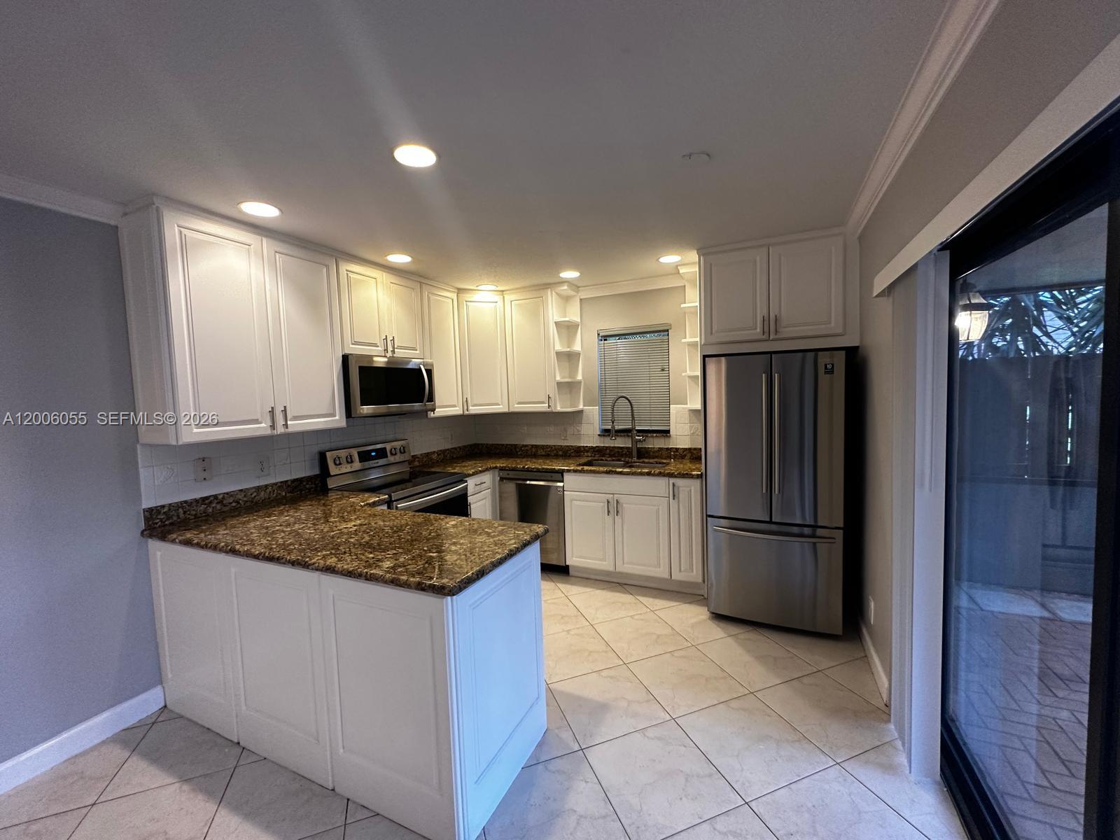 A kitchen features white cabinets, granite countertops, stainless steel appliances, and light-colored tile flooring — 7671 W Courtyard Run W, Boca Raton FL 33433, BOCA RATON, FL