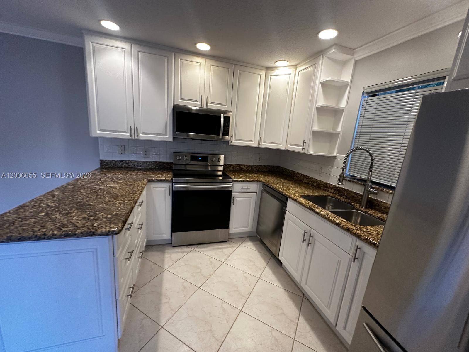 A kitchen features white cabinets, granite countertops, stainless steel appliances, and light-colored tile flooring — 7671 W Courtyard Run W, Boca Raton FL 33433, BOCA RATON, FL