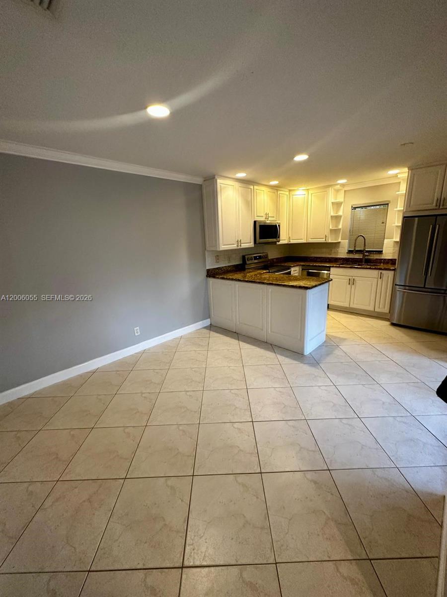 A kitchen with white cabinets, granite countertops, and tile flooring opens to a dining area — 7671 W Courtyard Run W, Boca Raton FL 33433, BOCA RATON, FL