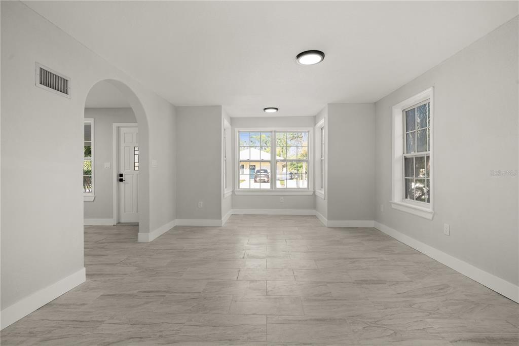 An empty room with light gray walls, tile flooring, a bay window, and an arched doorway — 309 BATH STREET, TARPON SPRINGS, FL