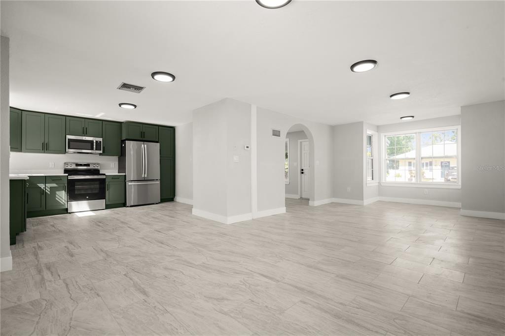 An open-concept kitchen and living area features dark green cabinets, stainless appliances, and light flooring — 309 BATH STREET, TARPON SPRINGS, FL