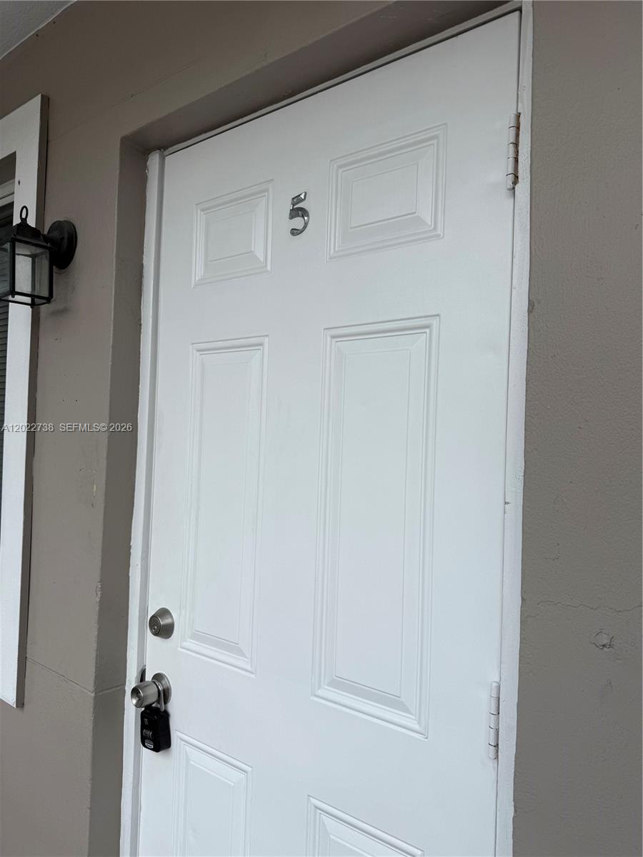 A white exterior door with the number five is mounted on a gray wall — MIAMI, FL