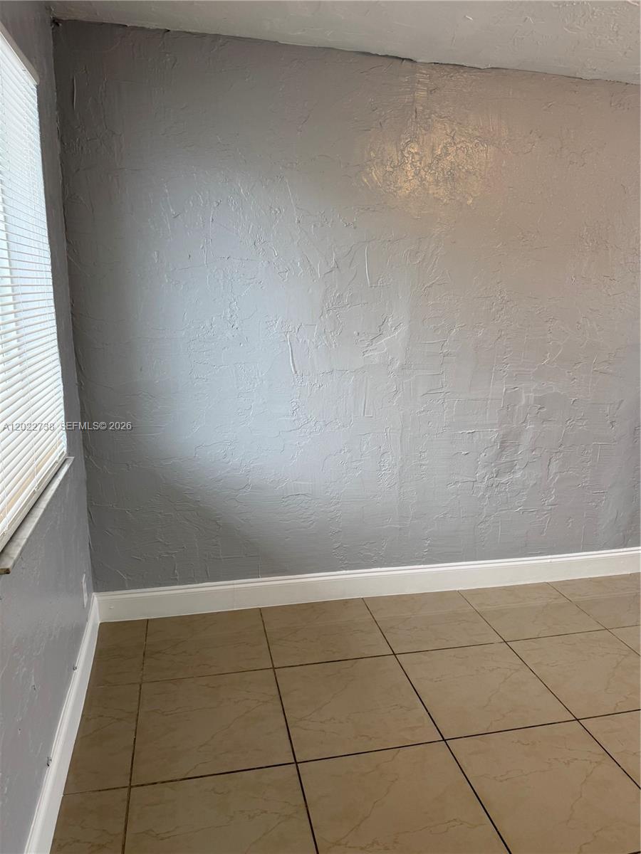 A room with light gray textured walls, white baseboards, and tan tiled flooring — MIAMI, FL