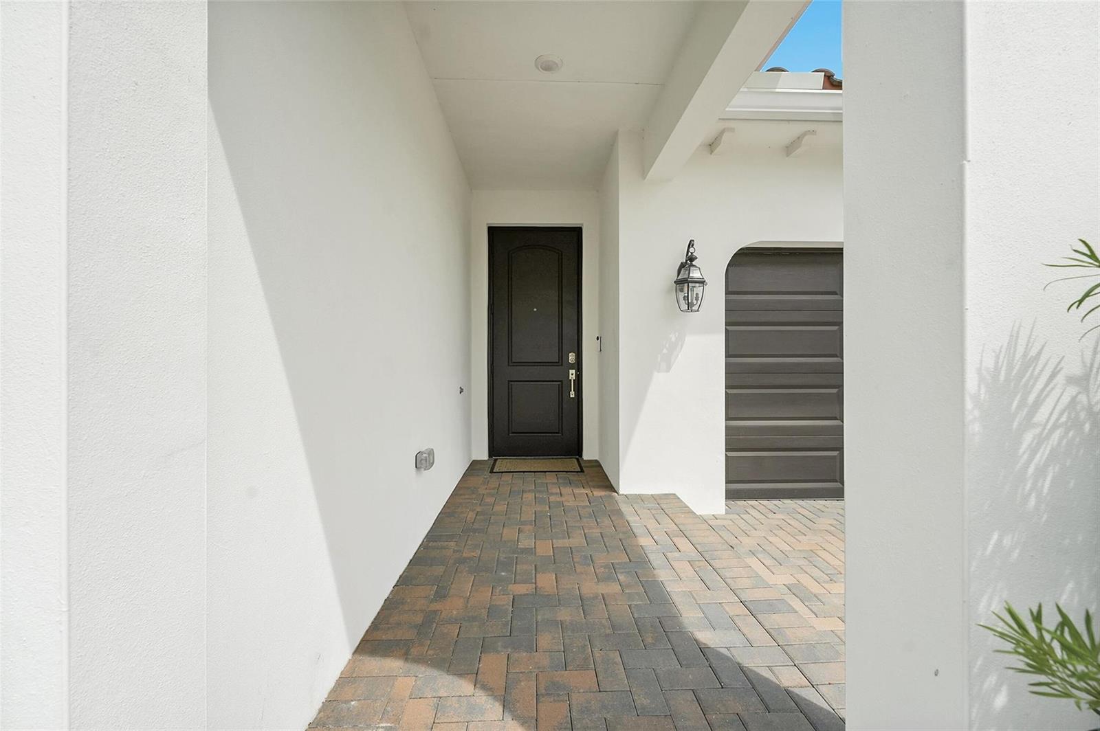 A covered entryway features a dark front door, a garage door, and paver flooring — 1878 Wandering Willow Way, FL 33470, FL