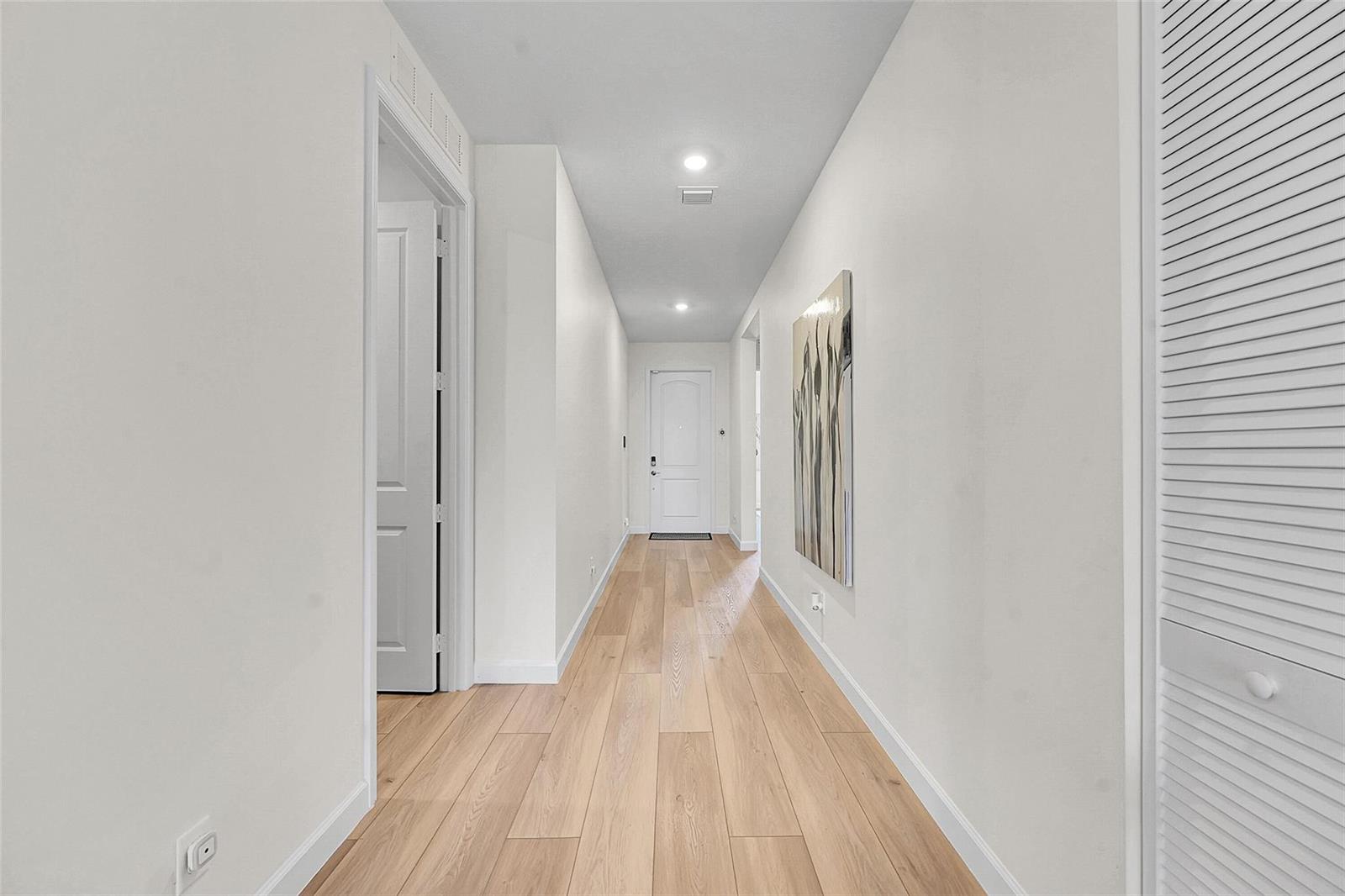 A bright hallway features light wood-look flooring, white walls, and a white door at the end — 1878 Wandering Willow Way, FL 33470, FL