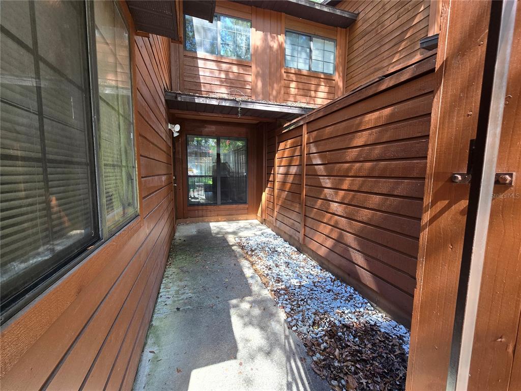 A narrow outdoor walkway features wood siding, a concrete path, and a gravel garden bed — 842 SW 55TH TERRACE, GAINESVILLE, FL