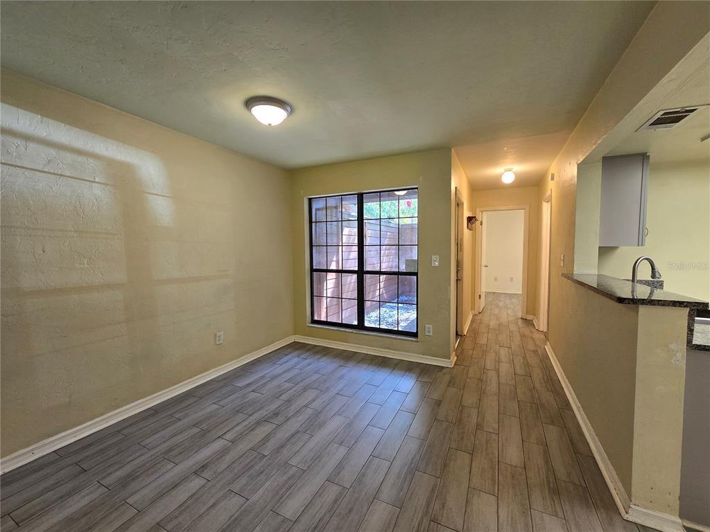 An empty dining area features wood-look tile flooring, a large window, and a kitchen pass-through — 842 SW 55TH TERRACE, GAINESVILLE, FL