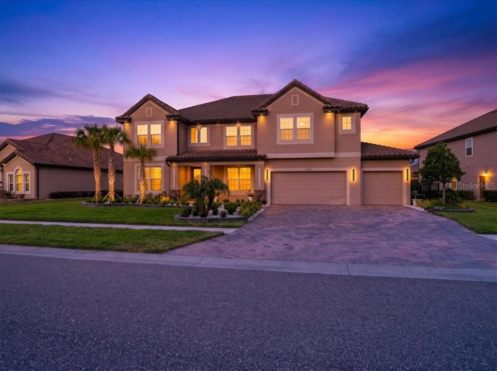 A two-story suburban house with a paved driveway and a three-car garage at sunset — 33239 KATELAND DRIVE, WESLEY CHAPEL, FL