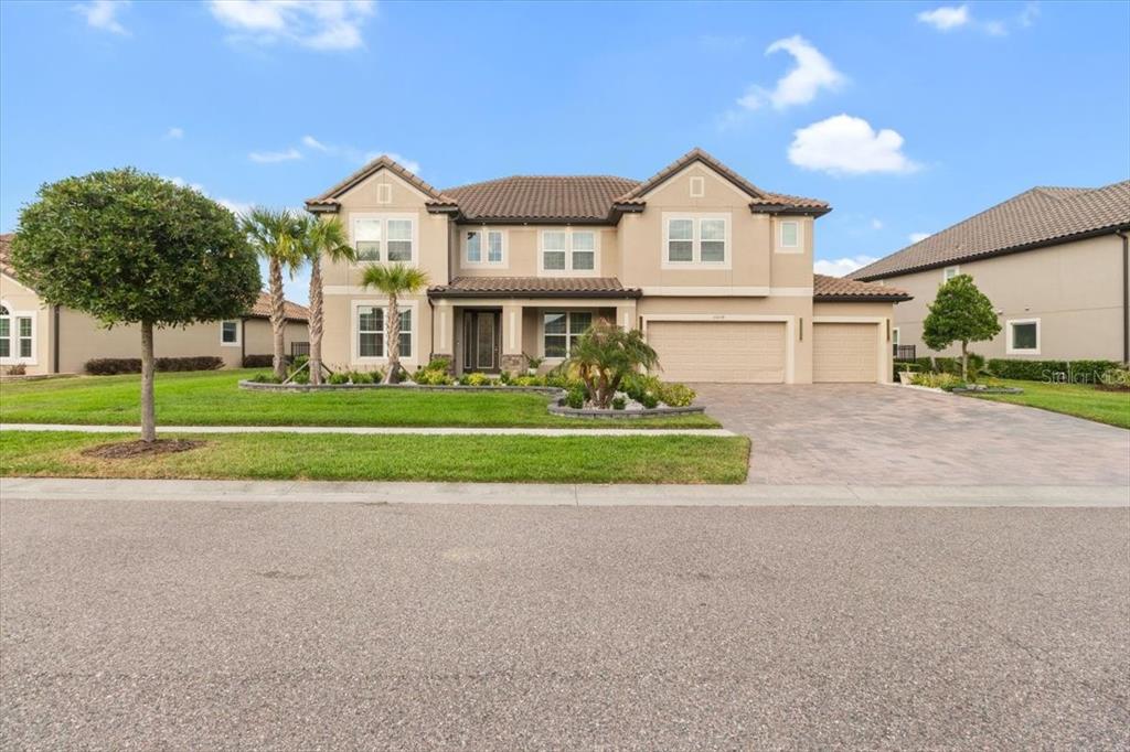 A two-story suburban house with a tan stucco exterior, tile roof, and three-car garage — 33239 KATELAND DRIVE, WESLEY CHAPEL, FL