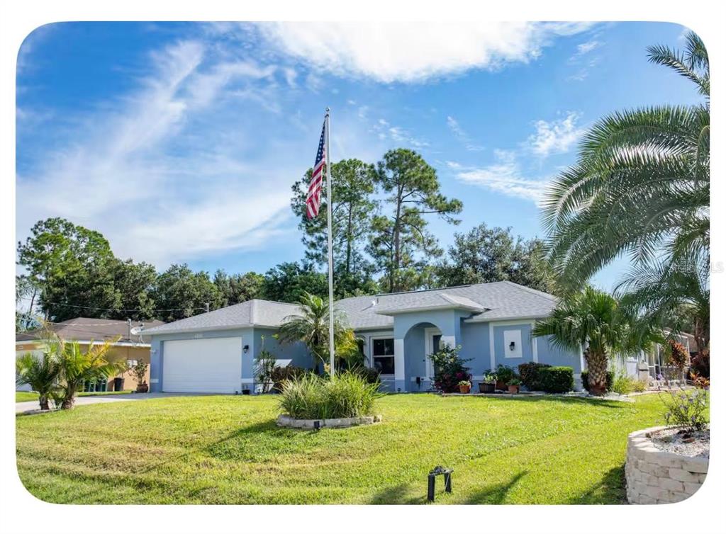 A light blue single-story house with a two-car garage and a tall American flag pole — 4568 THISBE STREET, NORTH PORT, FL