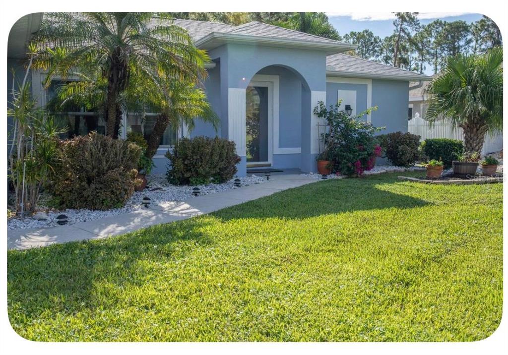 A blue single-story house features a covered arched entryway, a walkway, and landscaped front yard — 4568 THISBE STREET, NORTH PORT, FL