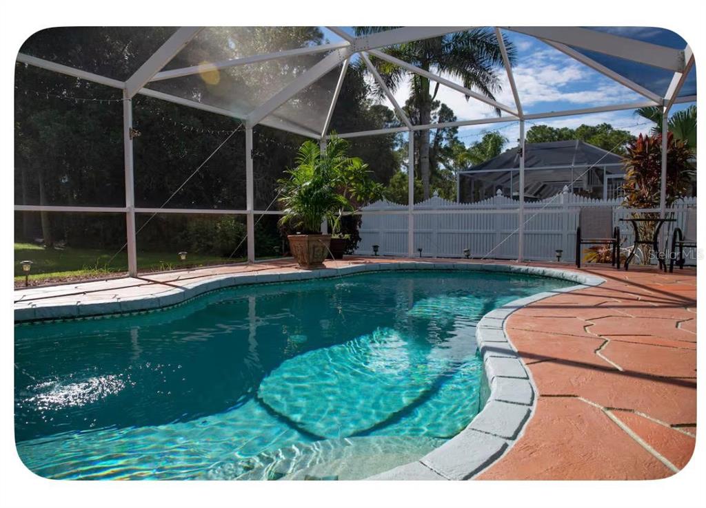 A screened-in swimming pool with a stone deck and a white fence in the background — 4568 THISBE STREET, NORTH PORT, FL