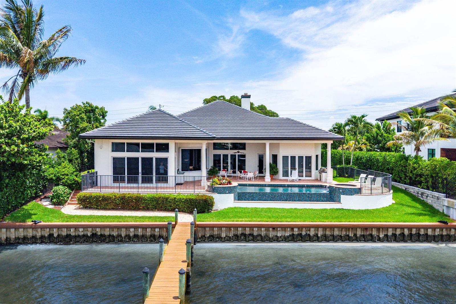 A waterfront house with a pool, patio, and wooden dock under a blue sky — 47 River Drive, Tequesta FL 33469, TEQUESTA, FL