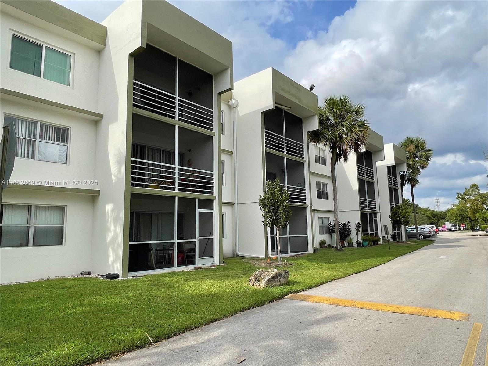 A multi-story white apartment building features screened balconies and a grassy lawn — 4255 N University Dr # 201, Sunrise FL 33351, SUNRISE, FL