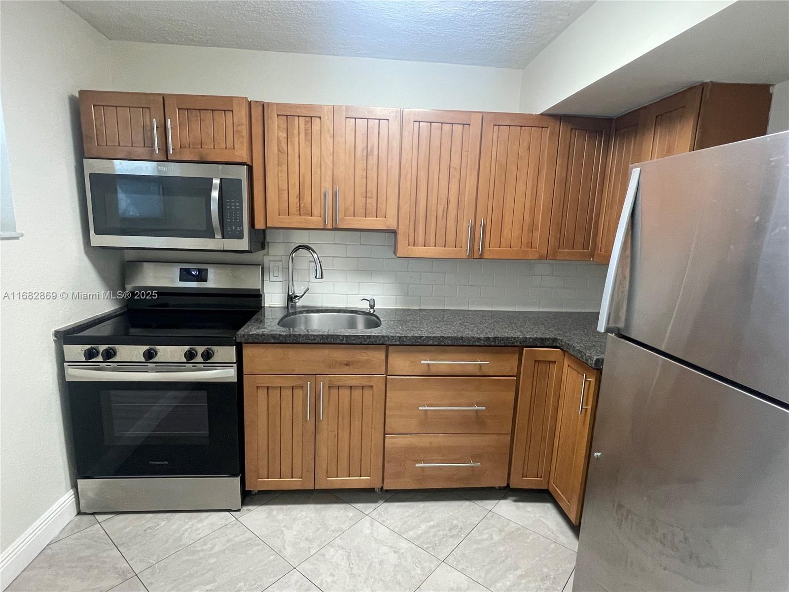 A kitchen features wood cabinets, stainless steel appliances, dark countertops, and a white backsplash — 4255 N University Dr # 201, Sunrise FL 33351, SUNRISE, FL