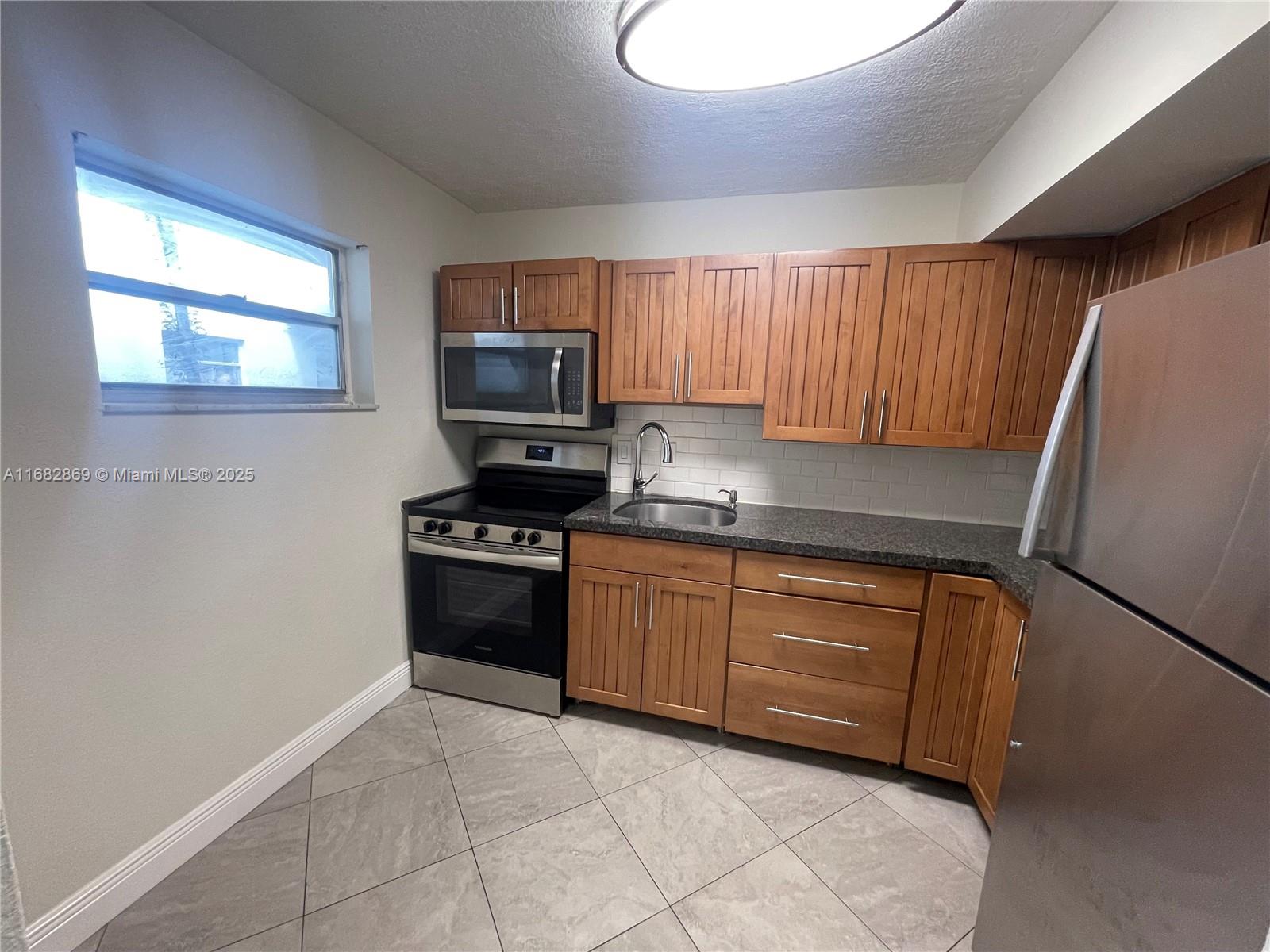 A kitchen features wood cabinets, stainless steel appliances, a tiled backsplash, and gray floor tiles — 4255 N University Dr # 201, Sunrise FL 33351, SUNRISE, FL