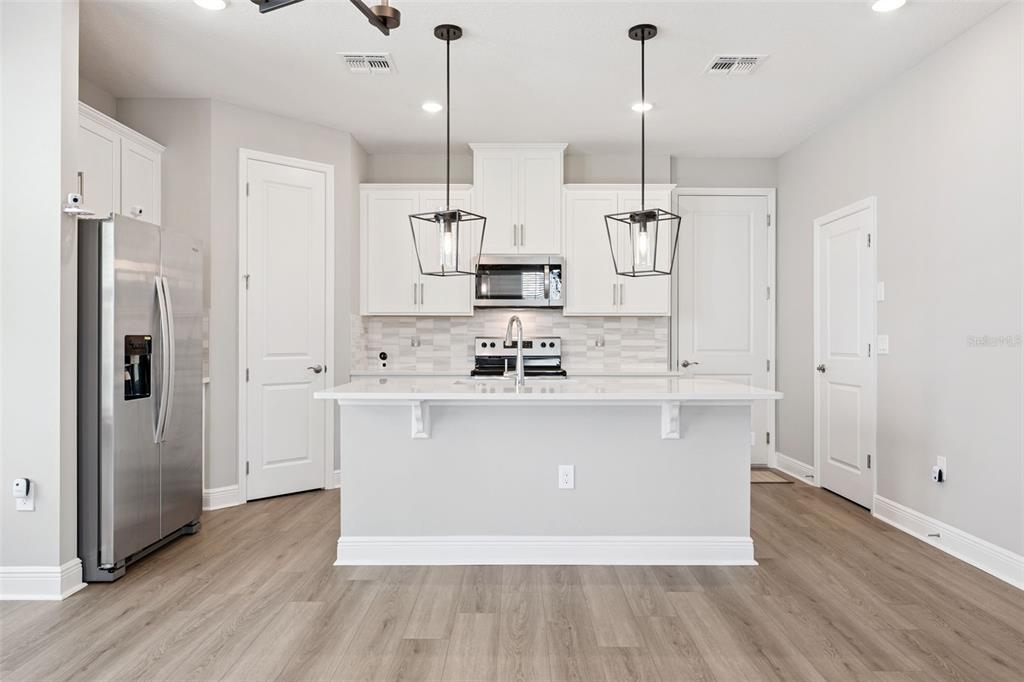 A modern kitchen features white cabinets, stainless steel appliances, a central island, and wood-look flooring — 12253 S BRACCO STREET, WINTER GARDEN, FL