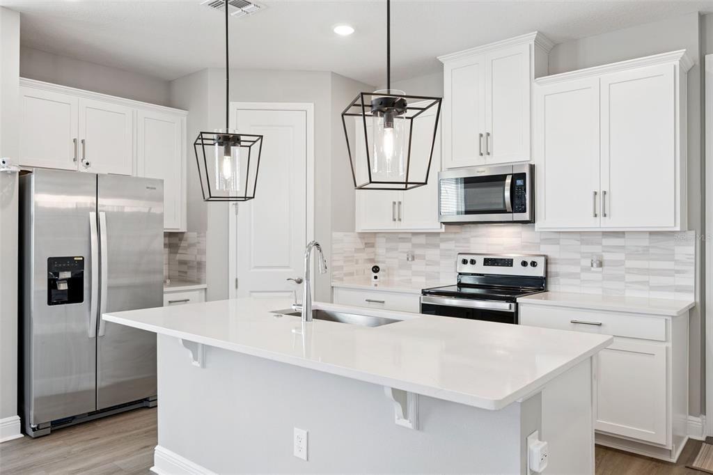 A modern kitchen features white cabinetry, stainless steel appliances, a quartz island, and pendant lighting — 12253 S BRACCO STREET, WINTER GARDEN, FL