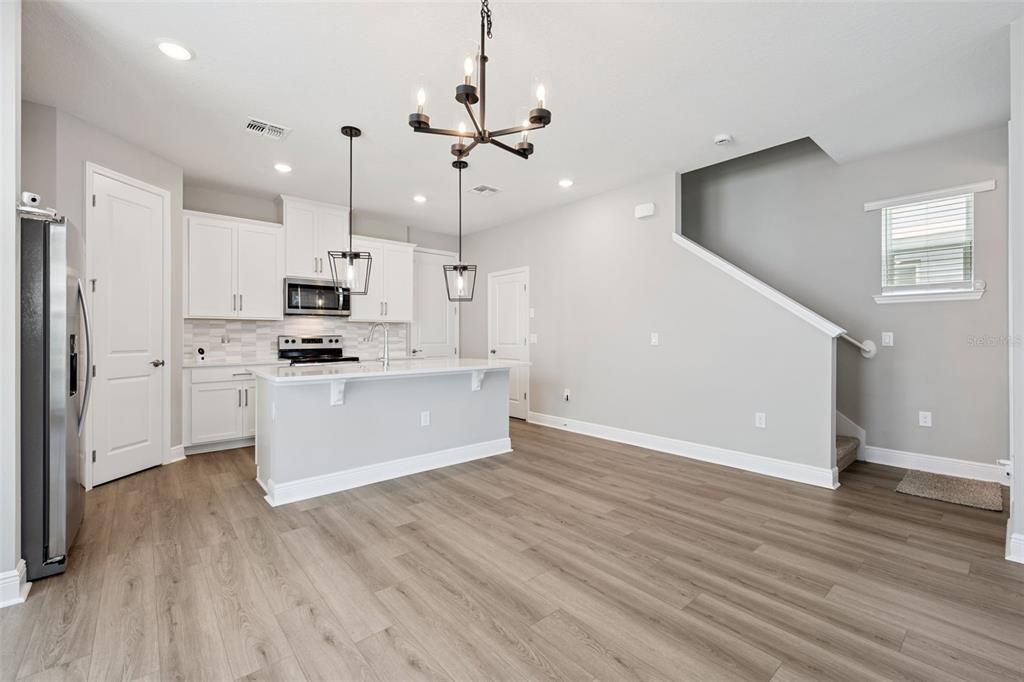 A kitchen with white cabinets, a center island, and wood-look flooring next to a staircase — 12253 S BRACCO STREET, WINTER GARDEN, FL