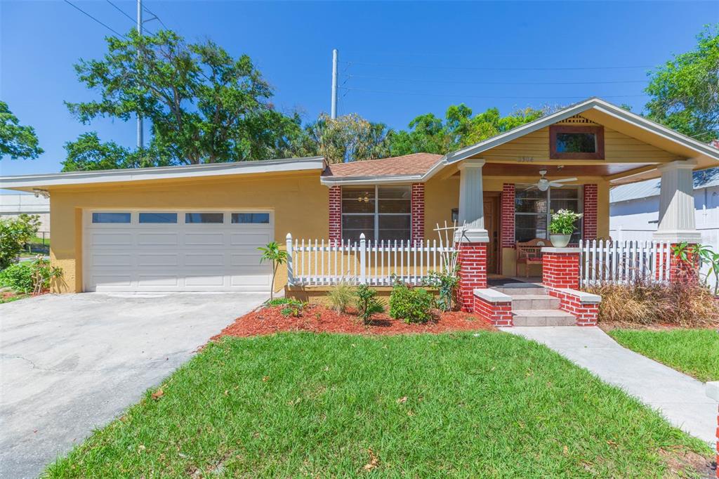 A yellow single-story house features a white garage door, a front porch, and brick accents — 2504 E 12TH AVENUE, TAMPA, FL