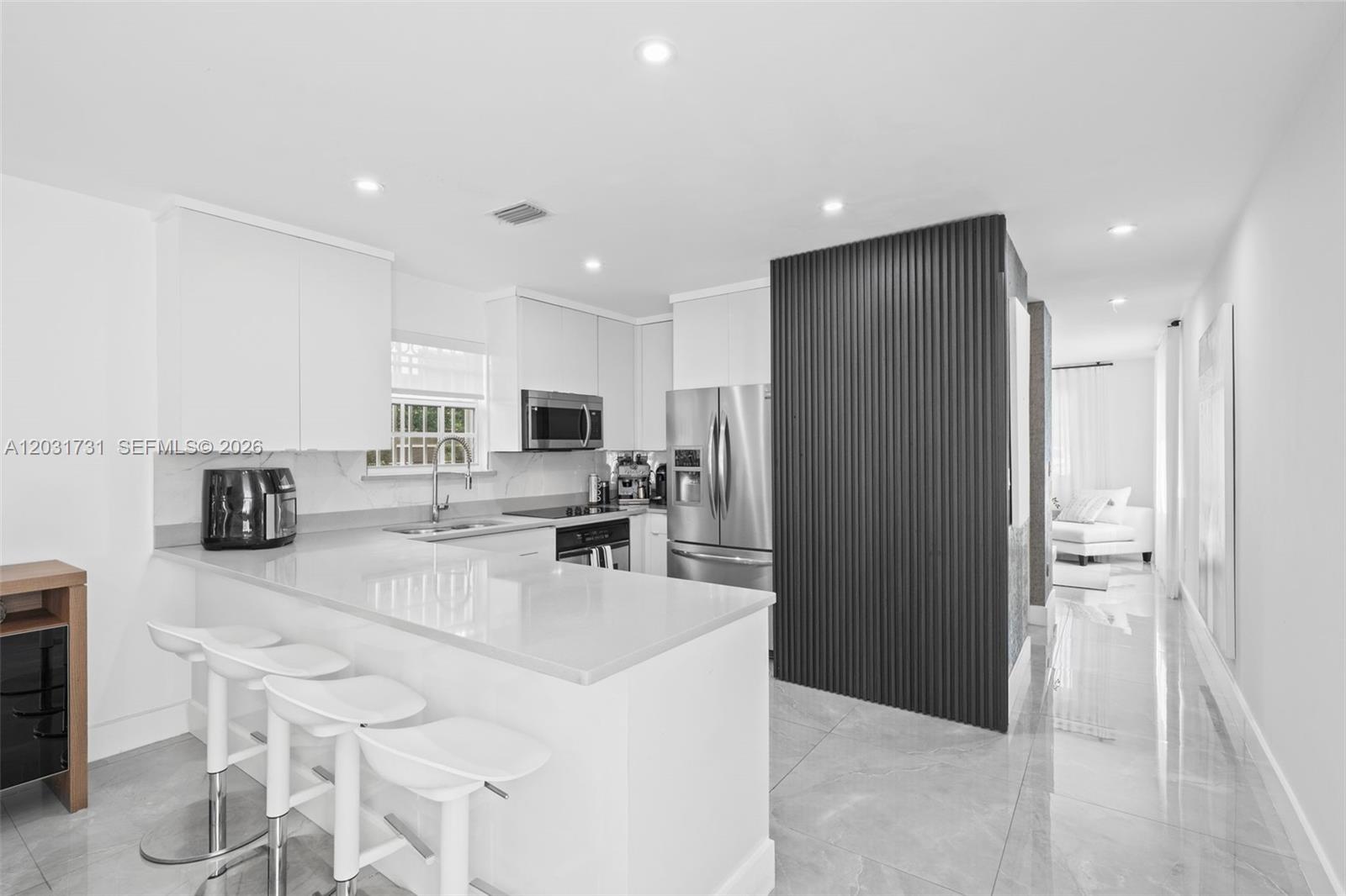 A modern kitchen features white cabinetry, a quartz breakfast bar, and a dark slatted accent wall — 2752 SW 11th St, Miami FL 33135, MIAMI, FL