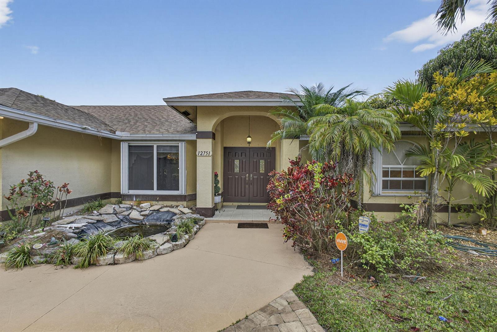 The exterior of a single-story house features a stone-lined pond, a paved walkway, and double doors — 12751 Orange Boulevard, West Palm Beach FL 33412, WEST PALM BEACH, FL