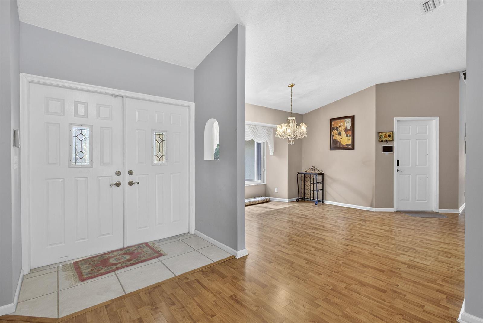 An entryway with tile flooring leads to a dining area featuring wood floors and chandelier — 12751 Orange Boulevard, West Palm Beach FL 33412, WEST PALM BEACH, FL